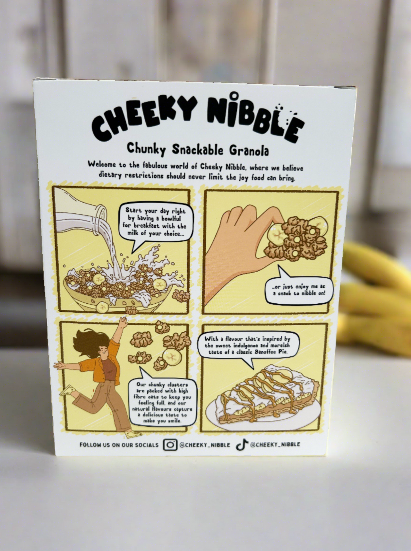 A whimsical cartoon illustration adorns the Banoffee Pie cereal box, featuring a cheerful banana character frolicking with a dollop of cream atop a slice of pie. The background showcases a sunny kitchen scene with scattered ingredients and a hint of a nostalgic bakery ambiance.