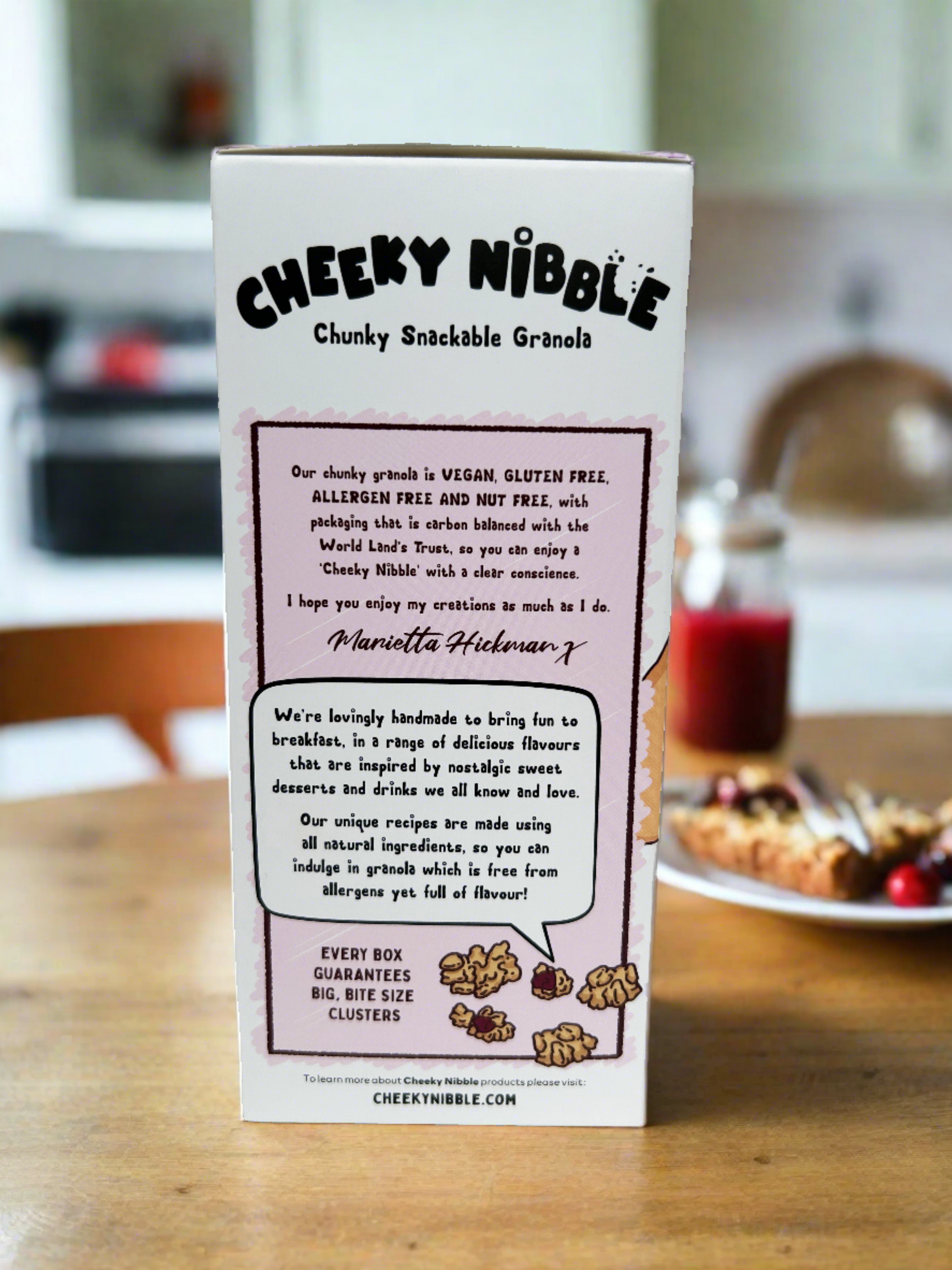 The cereal box showcases a close-up image of the mouthwatering granola chunks featured in Cherry Bakewell Granola. Each chunk is depicted with intricate detail, highlighting its hearty texture and flavorful blend cherries, and oats.  Text on the box may describe the crunchy, nutty sweetness of the granola, enticing consumers with promises of a delicious breakfast or snack option reminiscent of the classic dessert.