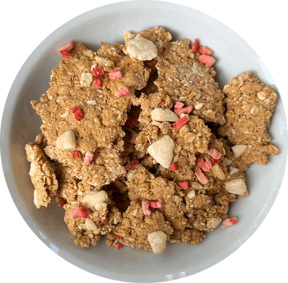 Image: A tempting bowl of Victoria Sponge granola, showcasing large, chunky pieces generously adorned with vegan white chocolate chips and scattered freeze-dried strawberry slices on top. The granola promises a satisfying crunch, while the white chocolate chips add a creamy sweetness. The vibrant red freeze-dried strawberries provide a burst of fruity flavor, reminiscent of the classic Victoria Sponge cake.
